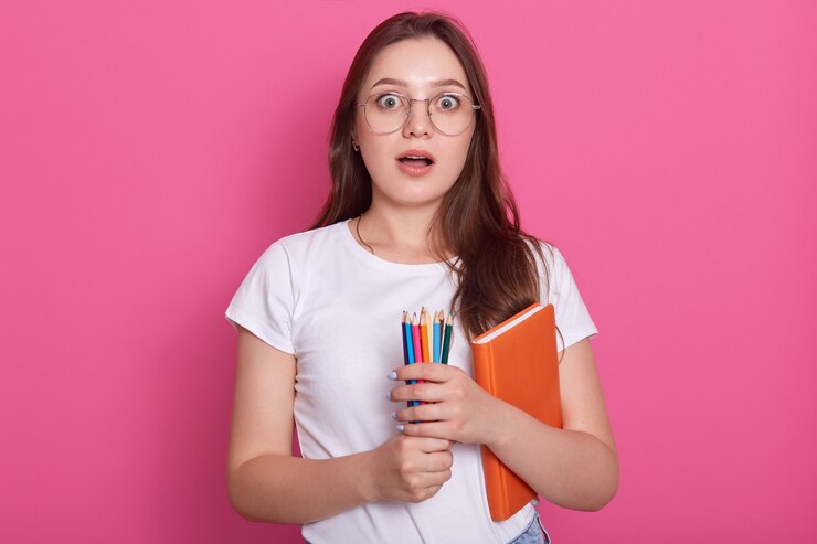 astonished-woman-with-opened-mouth-carries-textbook-colored-pencils-writing-drawing-being-ready-make-notes_176532-9673